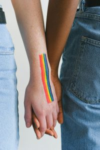 Two people holding hands with the pride / rainbow colours painted on the forearm of one of the people