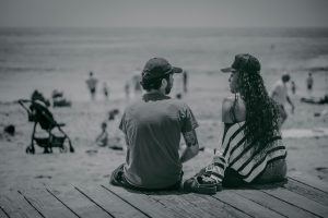 Black and white image of two people sat on a beach talking